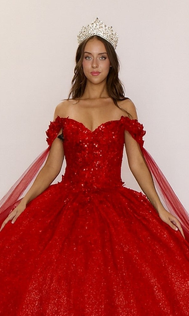 A woman wears the Quinceanera Dress Q127 by Nina Canacci—an off-the-shoulder, embellished red gown with a glitter tulle skirt and jeweled crown—standing against a plain background.